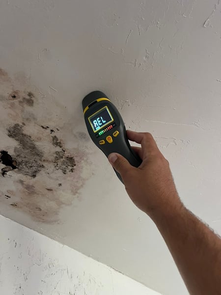 A hand holding a moisture meter on a ceiling, indicating very wet moisture levels