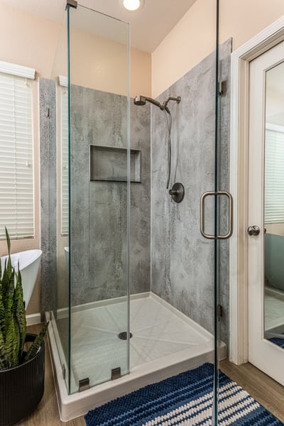 A walk-in shower with a clear glass enclosure and concrete colored walls