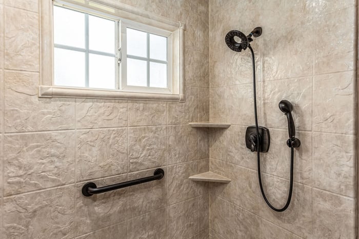 simulated tile pattern shower with a fixed head, removable head, two corner storage shelves, and a grab bar
