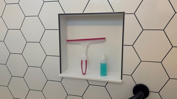 Inside a shower with a shower storage niche, holding a spray and squeegee