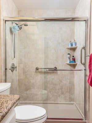 Tavertine wall walk-in shower with sliding glass doors.