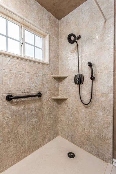 A walk in shower with a fixed and handheld shower head combo, two corner shelves, and a grab bar