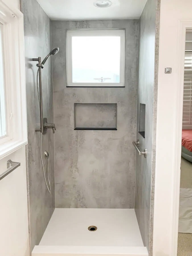 a walk-in shower with a grab bar and two shower niches