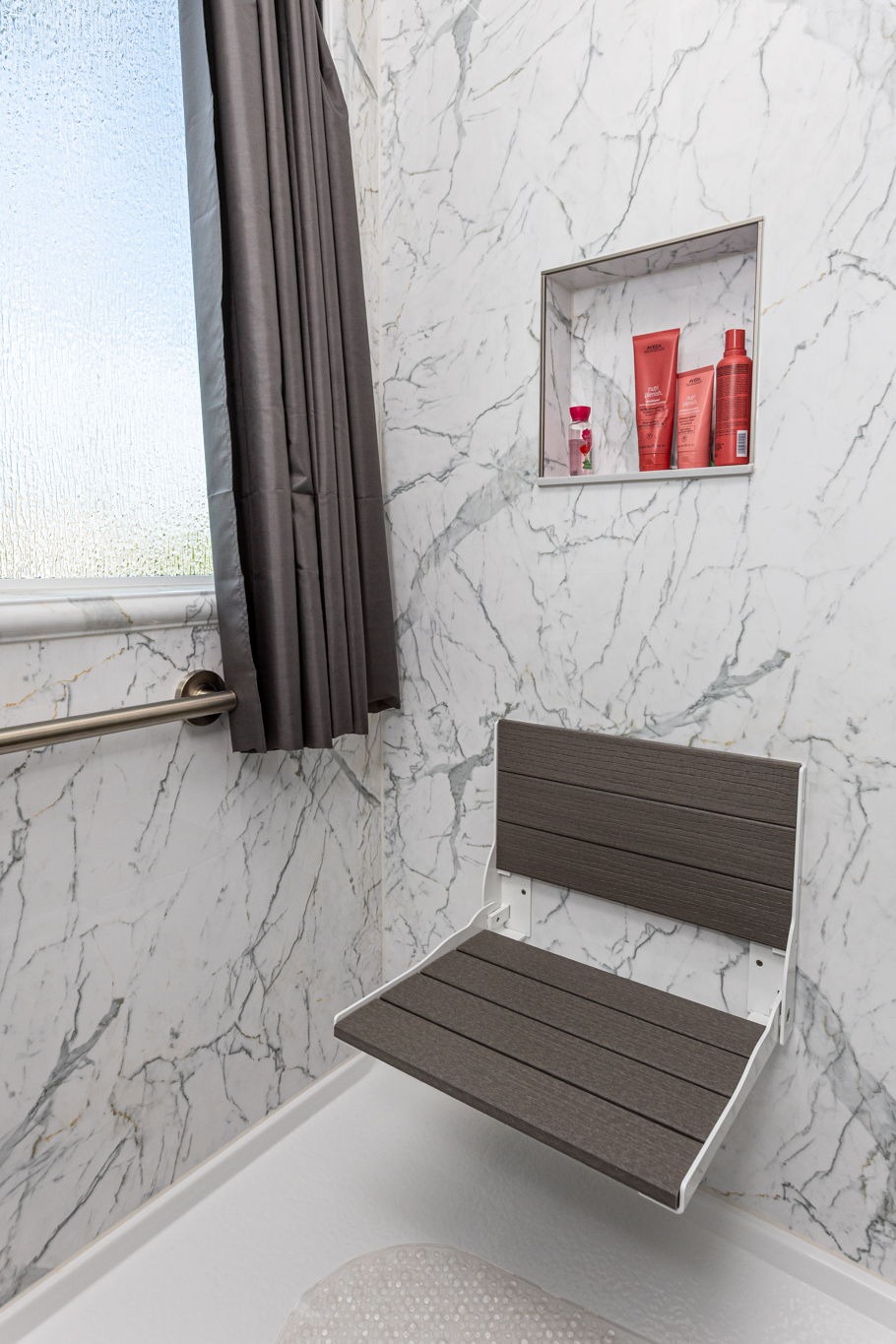 a walk-in shower with a grab bar, a folding seat, and a storage niche