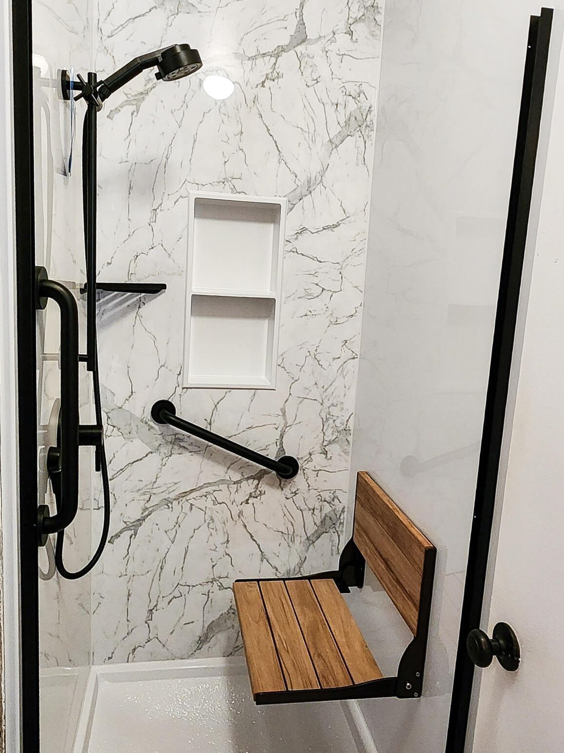 A walk-in shower with two grab bars, a storage niche, a corner shelf, and a folding shower seat