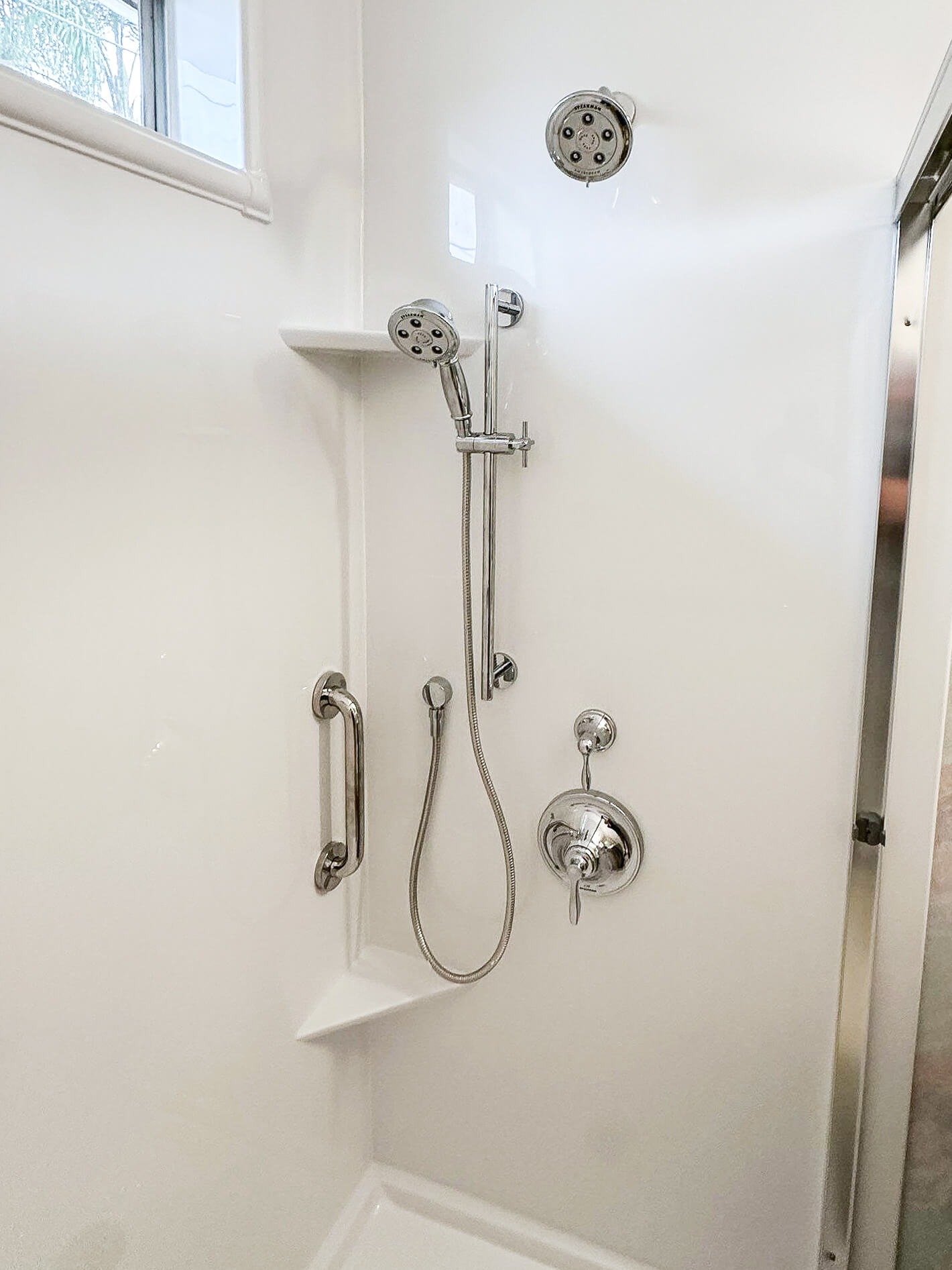 a walk-in shower with two corner shelves and a grab bar