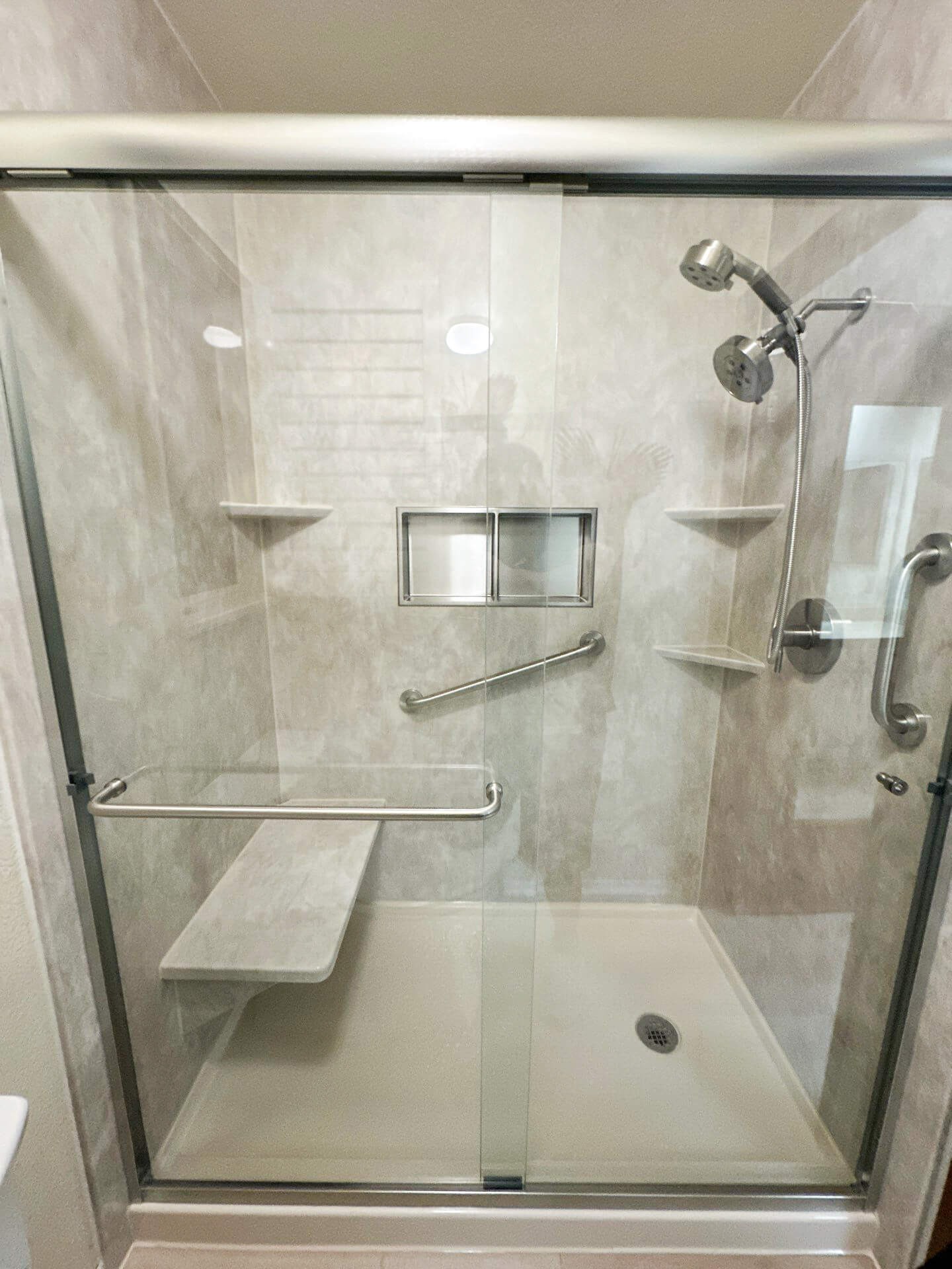 A walk-in shower with a shower bench, a storage niche, three corner shelves, and two grab bars