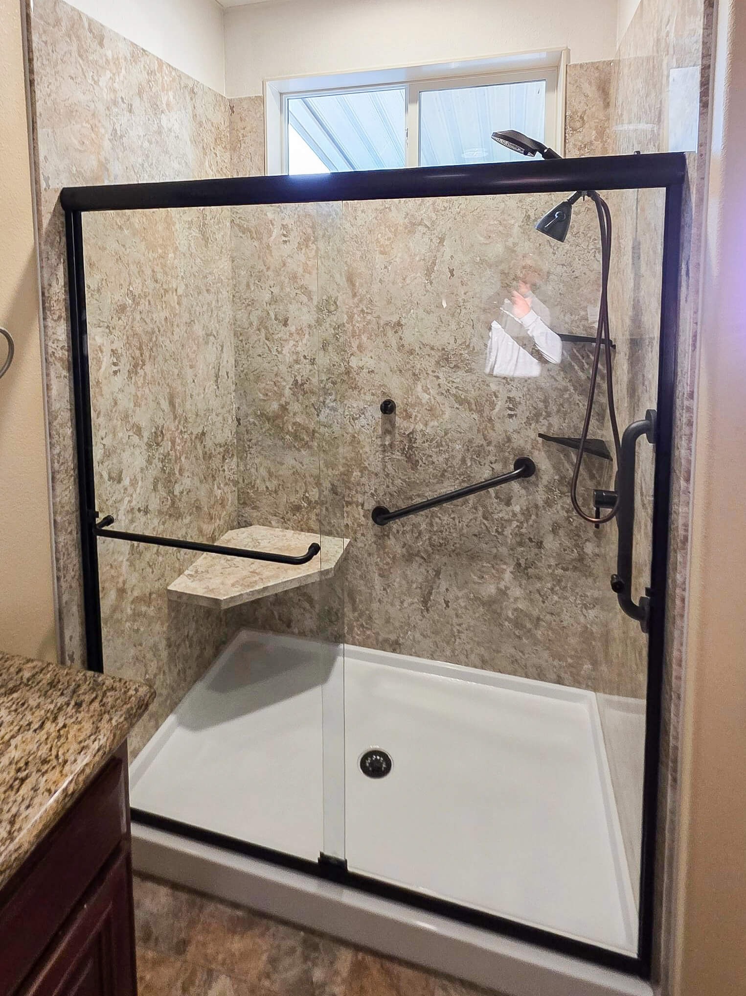 A walk-in shower with a corner seat, two grab bars, and two corner shelves
