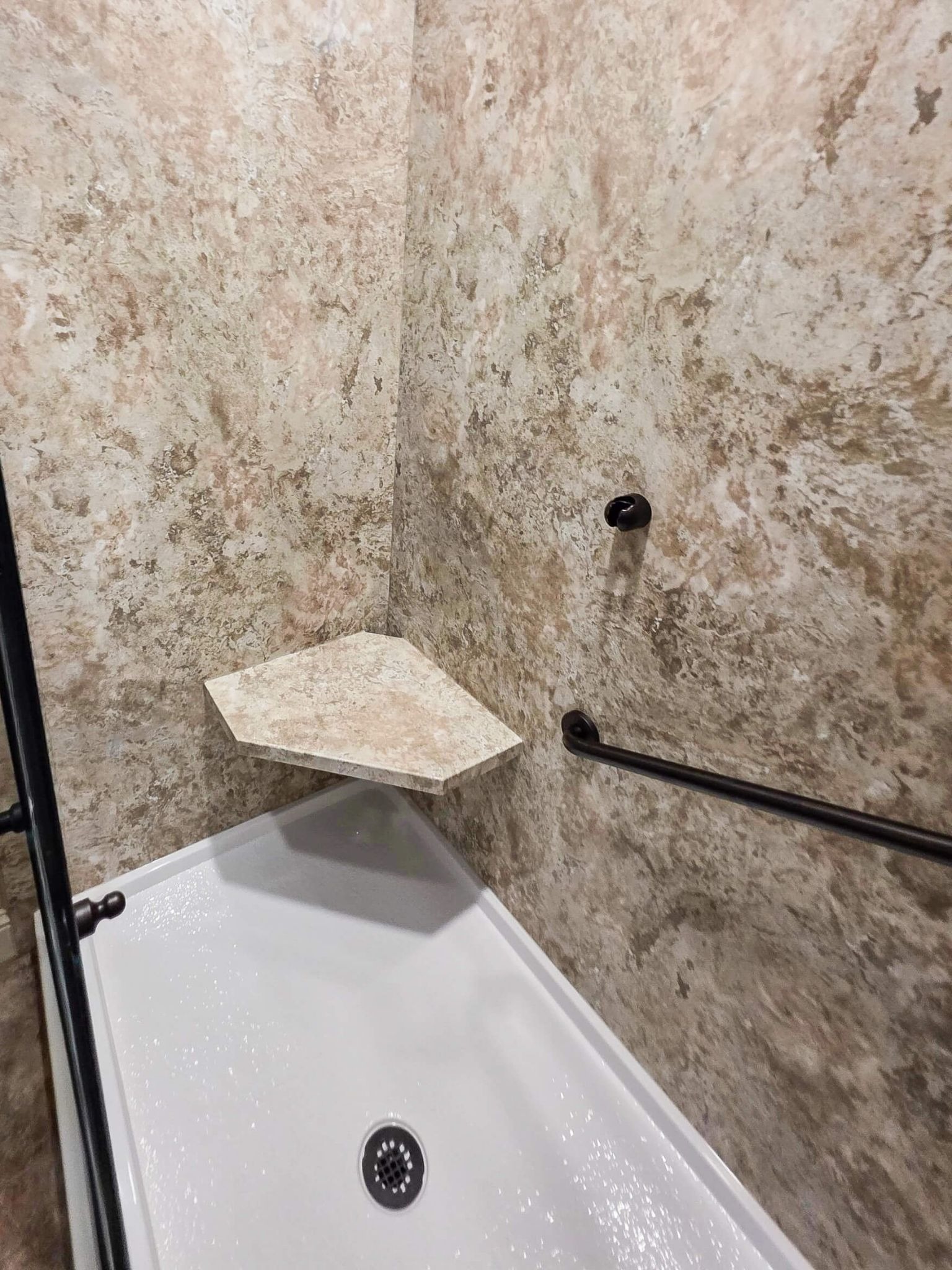 A walk-in shower with a grab bar and a corner seat